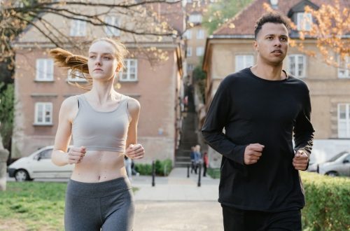 A young woman and man jogging on a city street during the day, wearing sportswear.